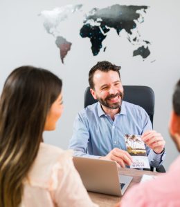 Attractive sales agent in a travel agency showing a couple of newlyweds a brochure with a tropical destination for their holiday vacation